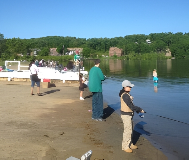 Kids lining up on the side of a lake with fishing rods